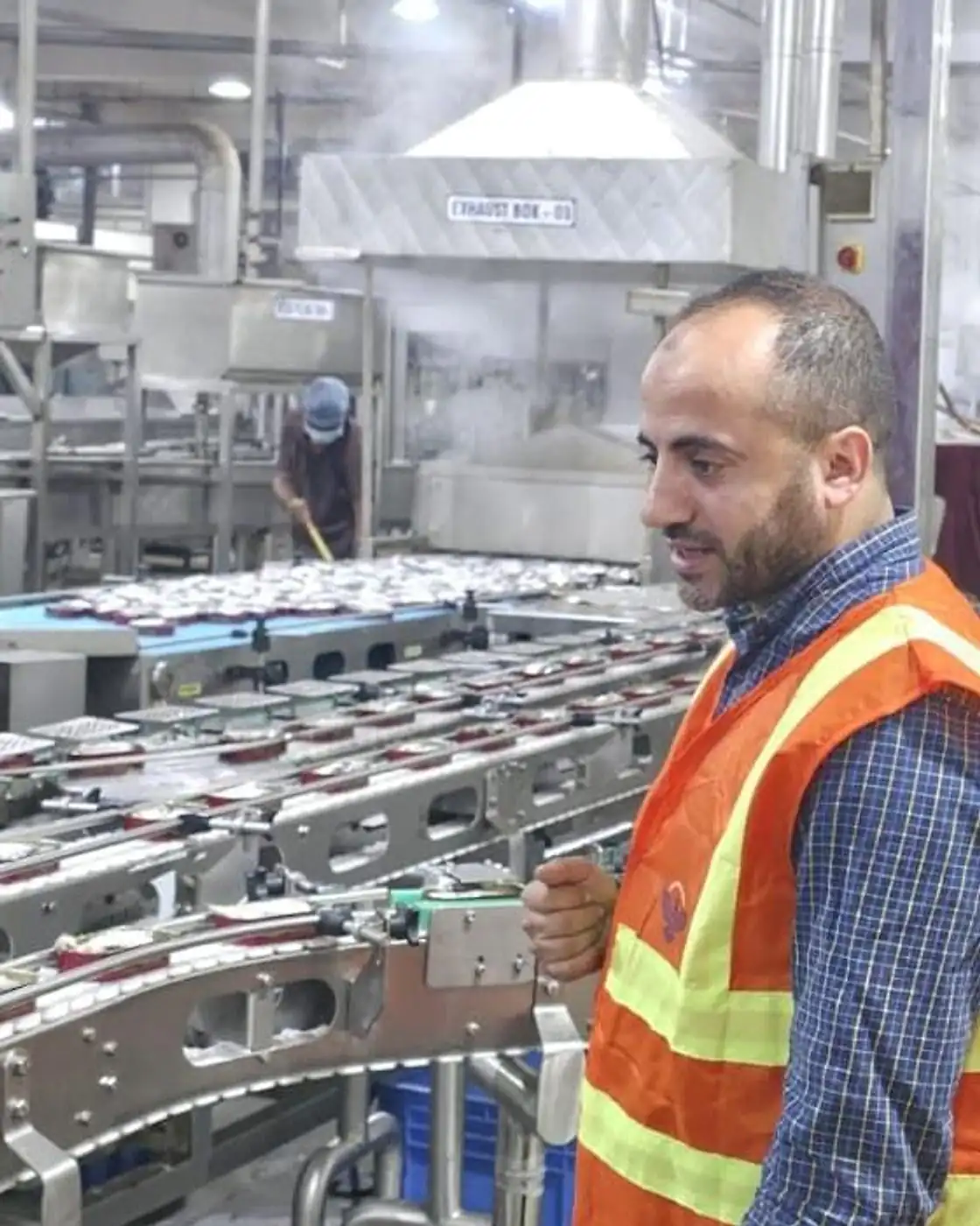 A team member in a high-visibility vest inspecting a food canning production line